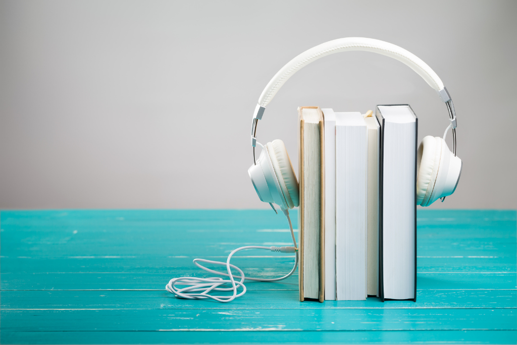 White headphones draped over a stack of books on a teal surface.