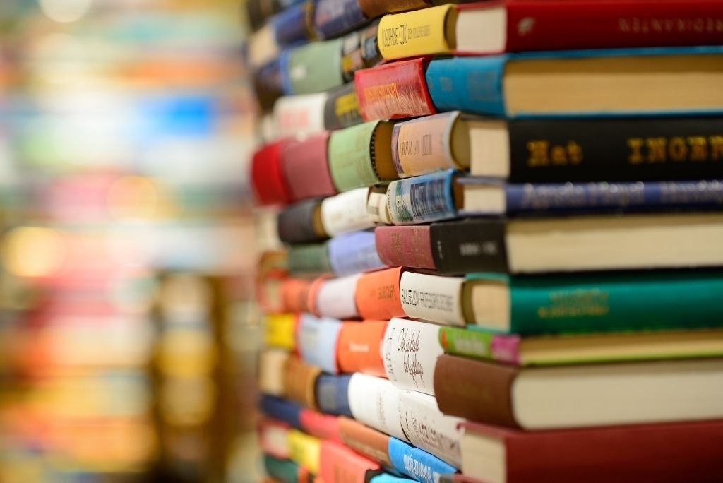 Close-up of a stack of various colorful books with a blurred bookshelf in the background.