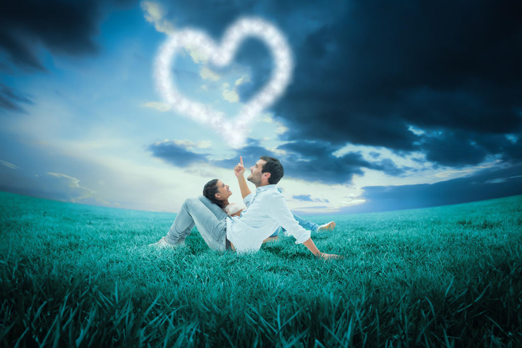 Couple lying on grass pointing at a cloud heart in a stormy sky.