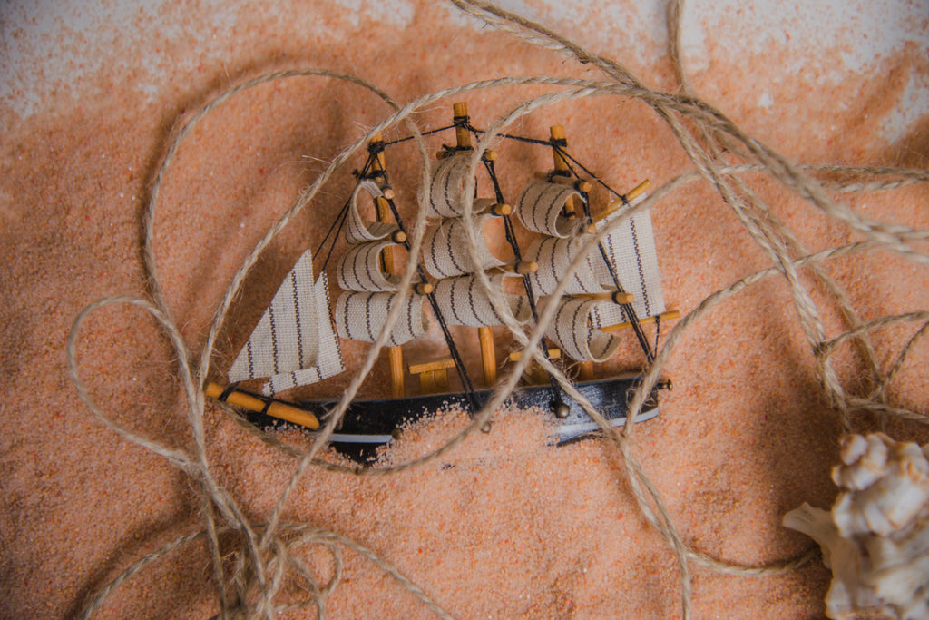 Miniature ship model entangled in string with sandy background and seashell.