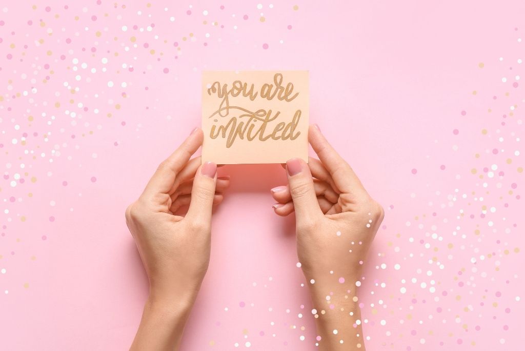 Hands holding a "you are invited" card against a pink background with confetti.