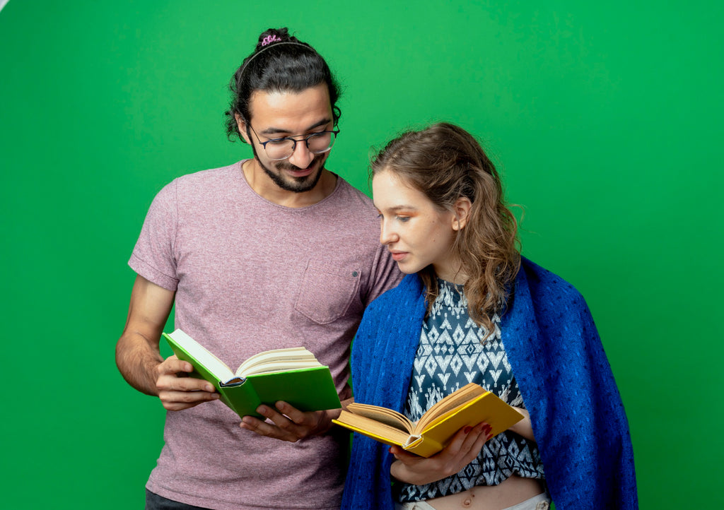 Two people reading books together, smiling against a green backdrop.