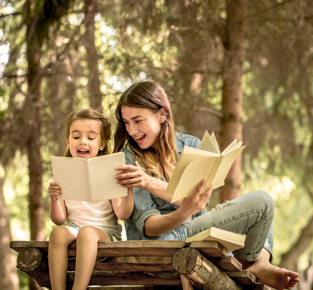 Adult and child reading together on a wooden bench in nature.