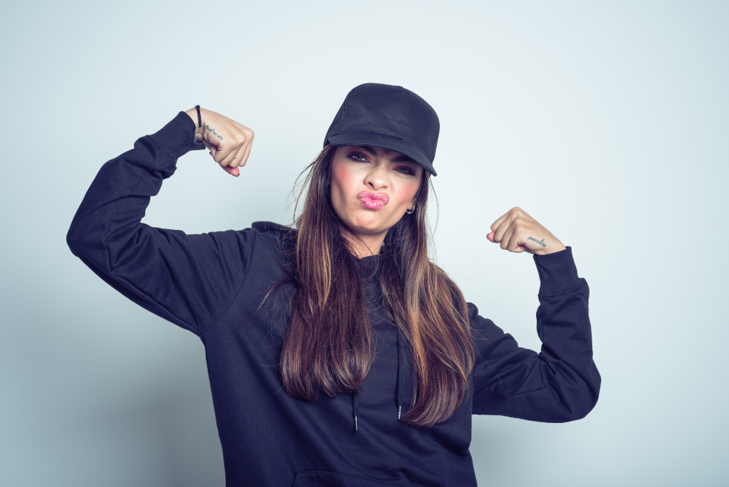 Confident woman flexing muscles, wearing a cap and making a funny face