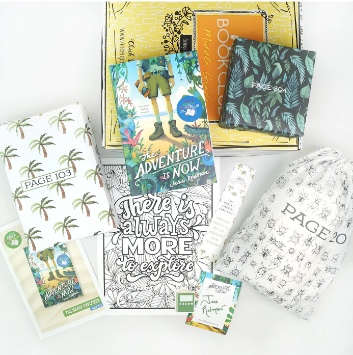 A display of "Once Upon a Book Club" box contents with the book "The Adventure is Now" by Jess Redman, themed gifts wrapped with page numbers, and a quote "There is always more to explore", inviting interactive reading.