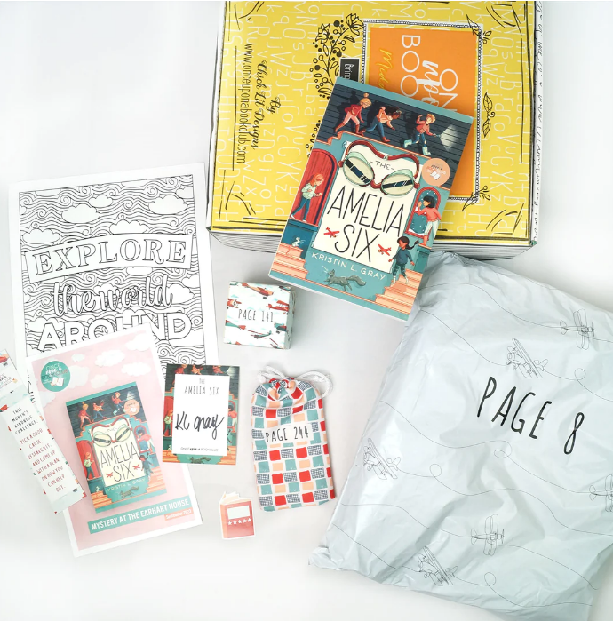 A creative layout of "Once Upon a Book Club" box contents, featuring the book "The Amelia Six" by Kristin Gray, along with uniquely wrapped gifts linked to specific pages, ready to offer a thematic reading experience.