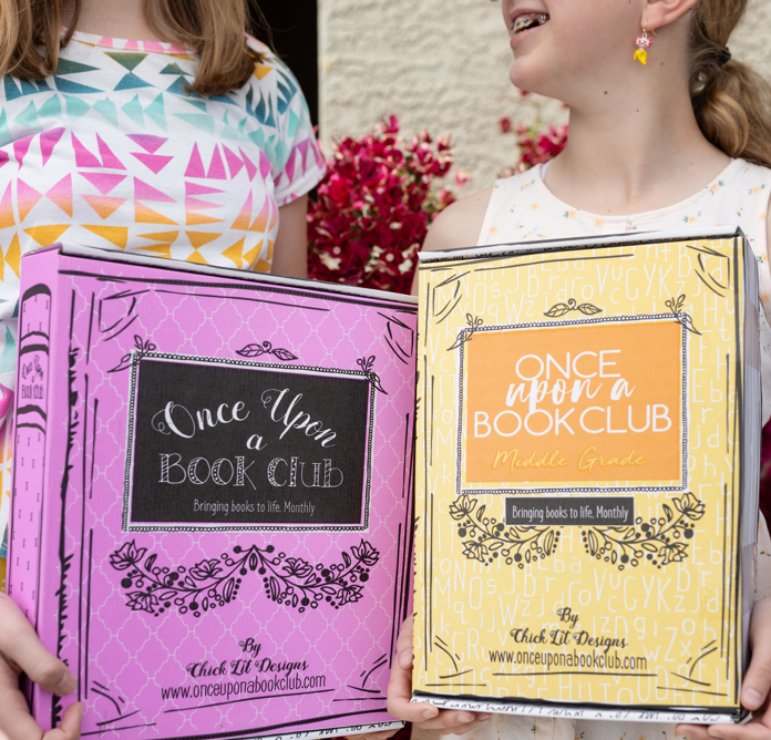 Two smiling girls holding "Once Upon a Book Club" boxes, one pink and one yellow, both labeled 'Middle Grade', celebrating the joy of a monthly book subscription service designed for young readers.