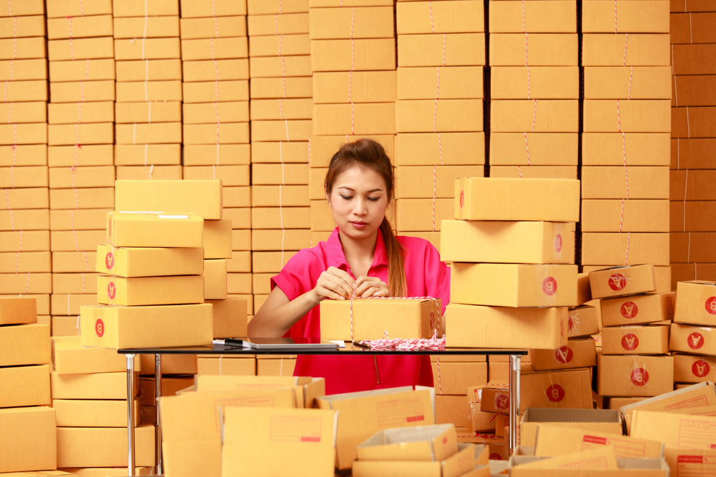 Worker packaging boxes in a warehouse filled with stacked parcels.