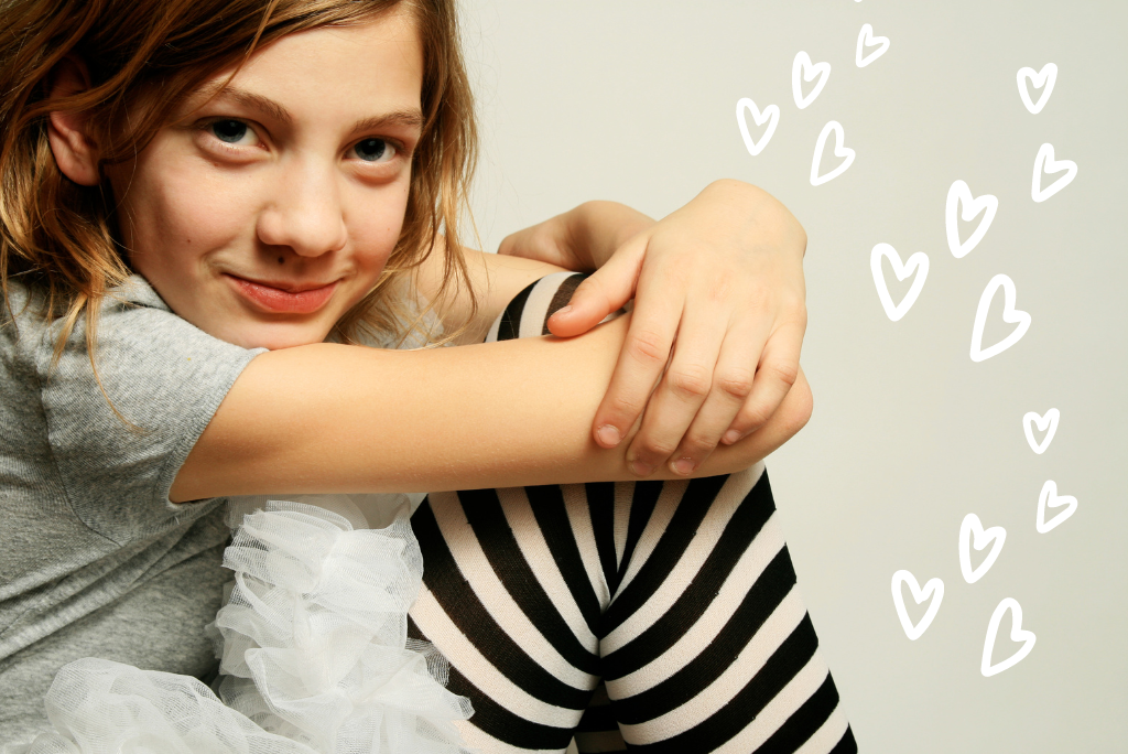 A smiling young person hugging their knee with drawn hearts.