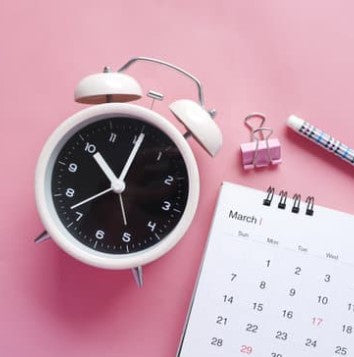 A clock, calendar, paper catcher, and a pen with pink background.