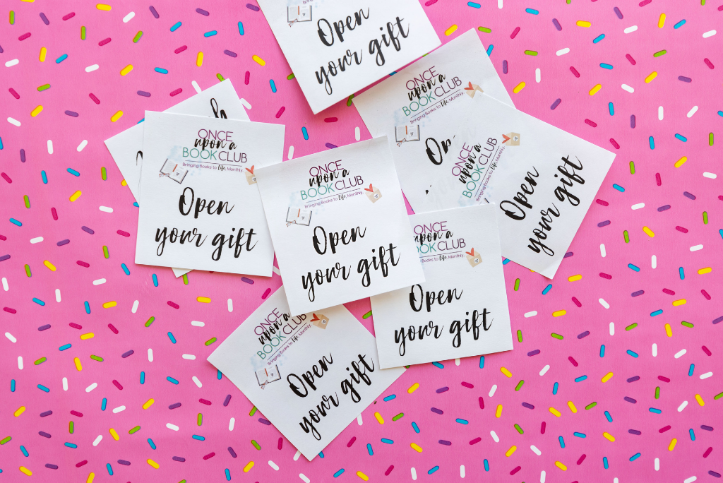 Cards saying "Open your gift" from a book club on a sprinkled pink background.