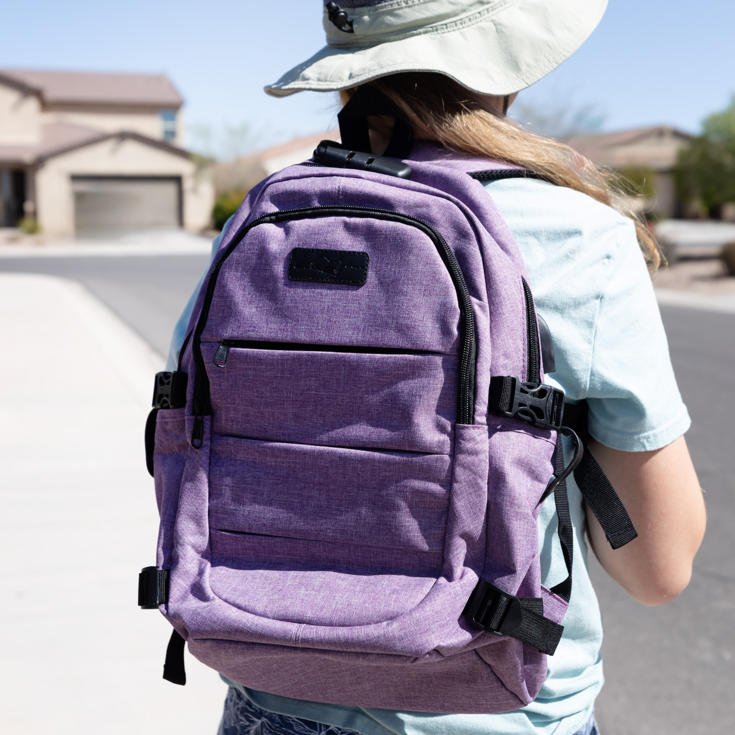 A white child facing away from the camera wears a purple backpack on her back.