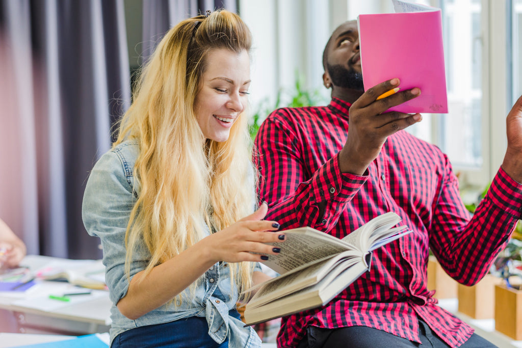 Two people laughing, sharing a moment with a pink notebook and a book in a bright room.