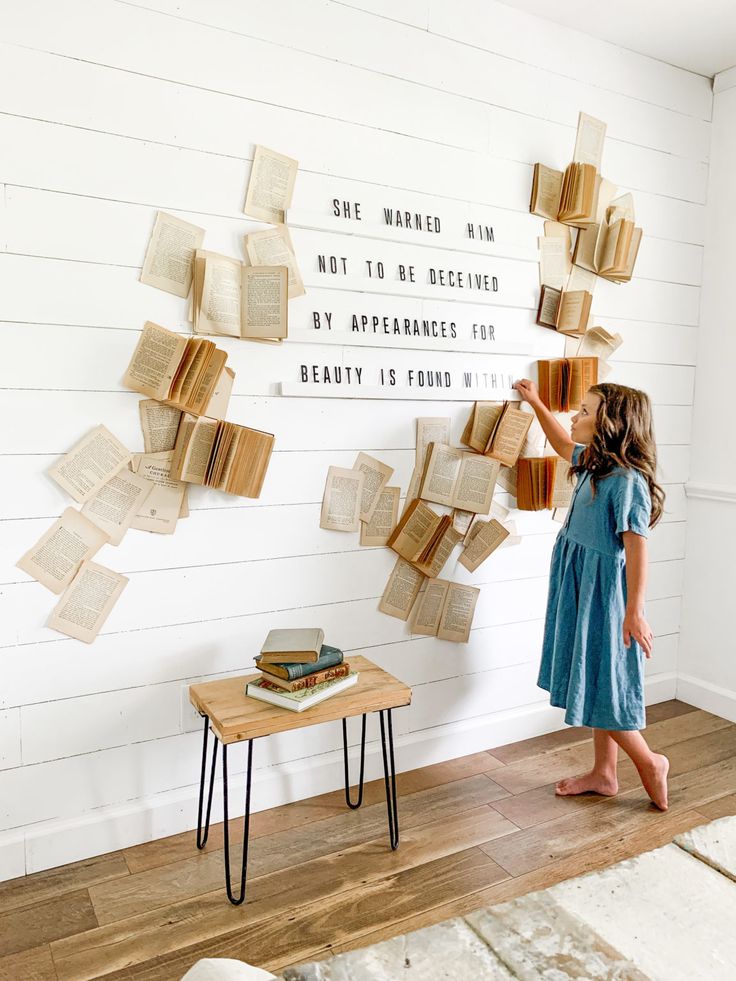 A girl writes, 'She warned him not to be deceived by appearances for beauty is found within...' on the wall surrounded by opened books with flattering pages.