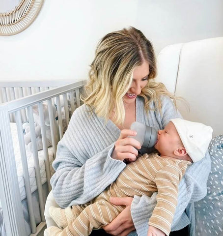 Woman sitting in chair bottle-feeding baby