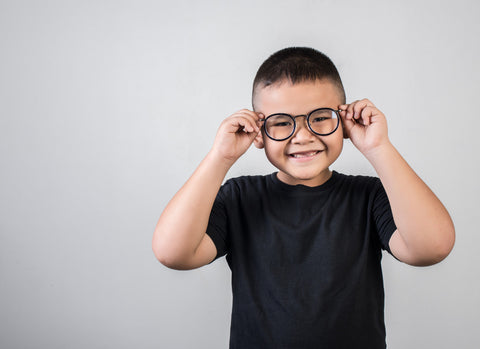 como escolher óculos infantil: criança oriental sorrindo com seus óculos e camisa preta num fundo cinza