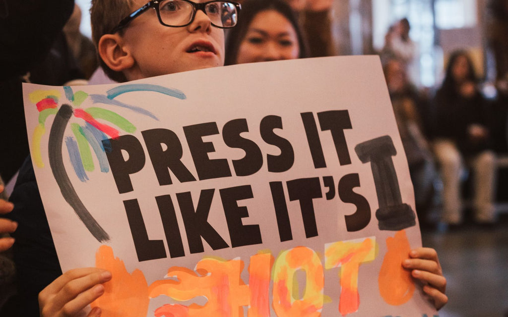 Boy holding up a sign that says Press It Like It's Hot.