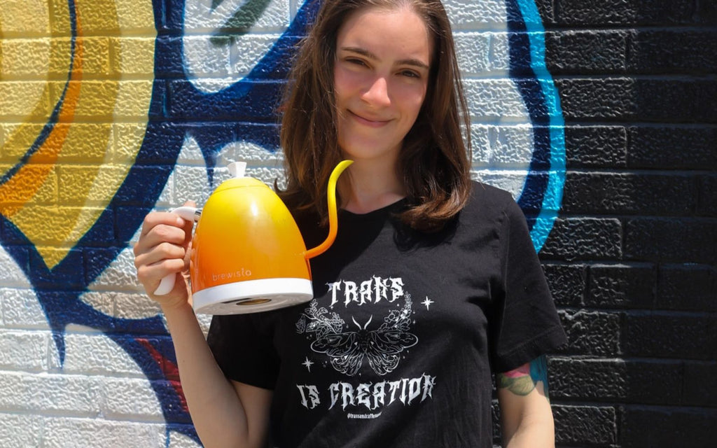 Arielle Rebekah is holding the Artisan Kettle in Candy Orange in front of a wall mural.