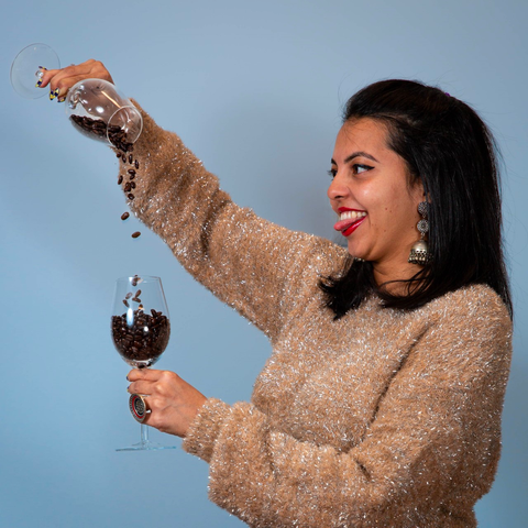 Divya Raghavan pours coffee beans into a wine glass filled with coffee.