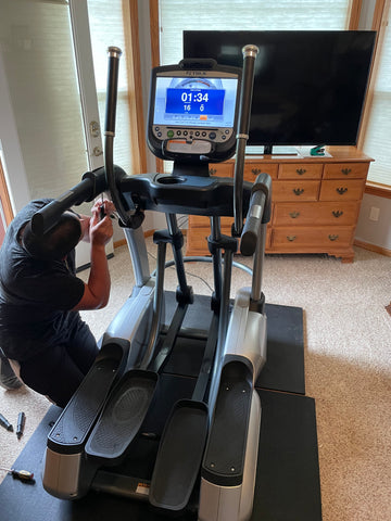 A service technician at Express Gym Supply working on an elliptical