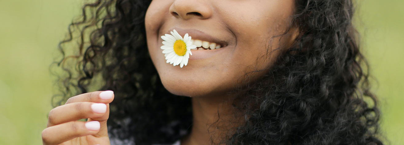 Black Woman smiling with a flower in her lips.