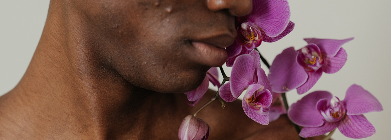 Black man with some visible acne, with a purple orchid against his skin.