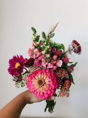 A bouquet of flowers - hot pink, cranberry, and light pink - held up against a beige wall