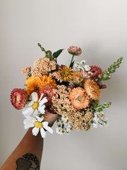 A bouquet of flowers - peach, white, orange - held up against a beige wall