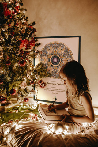 Kislány egy karácsonyfa és egy mandala előtt karácsonyi levelet ír