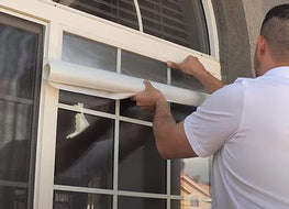 an installer is using a plastic squegee to press the window film in place on the exterior of the window