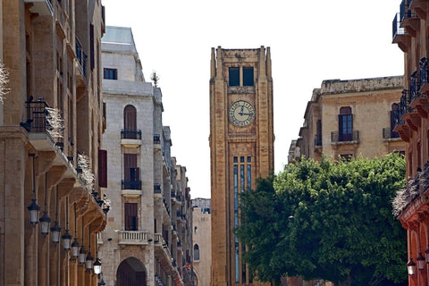 A picture showing downtown Beirut, with buildings in the foreground, a tree top on the right and a clock tower in the back.