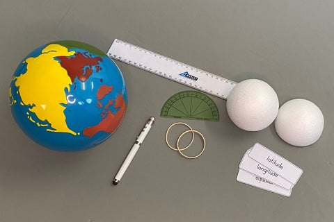 Time Zone Presentation: 3.a - Introducing Latitude and Longitue (On the left, there is the Montessori continent globe. In the middle, there is a torch, a ruler, a protractor and some rubber bands. On the left, a whole styrofoam ball and a half styrofoam ball above latitude and longitude labels.)