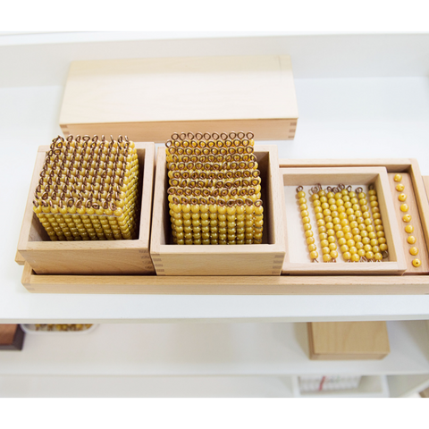 Montessori golden beads on a tray. From left to right: one thousand-cube, nine hundred-squares, nine ten-bars and nine unit-beads.