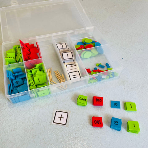 A tackle box on a blue floor that contains foam squares in red (100), blue (10) and green (1000, 1). Montessori stamp game.