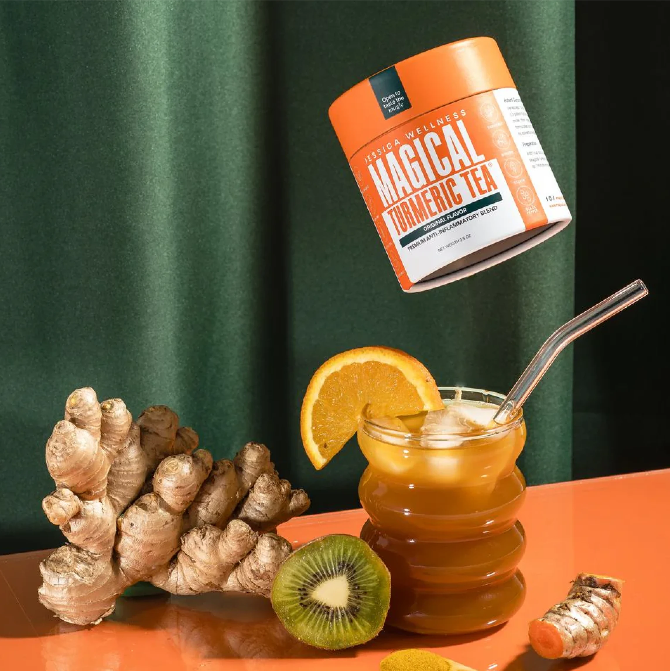 A jar of turmeric tea beside fresh ginger, kiwi, and a glass of iced tea with an orange slice.