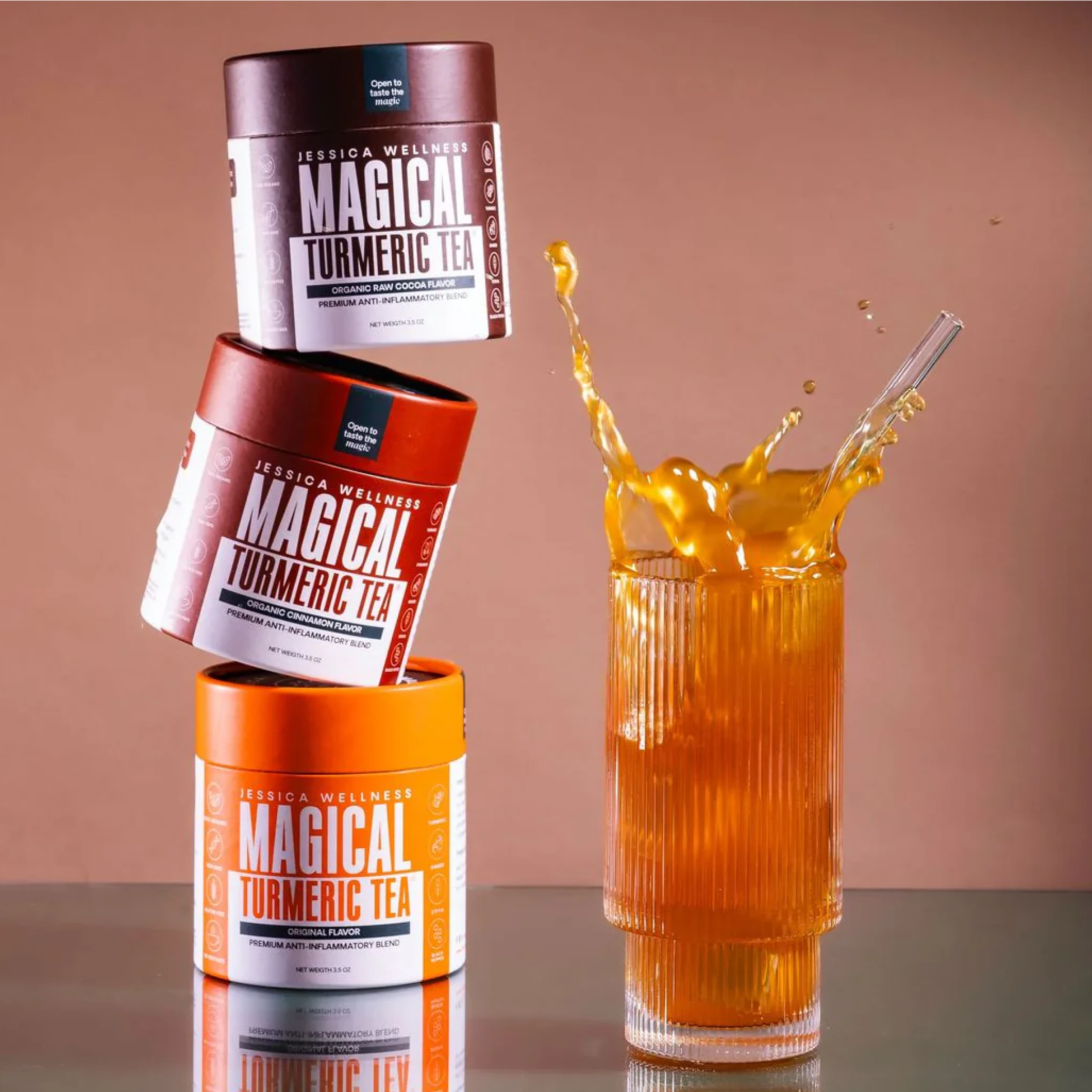 Three stacked turmeric tea containers beside a glass of splashing turmeric tea.