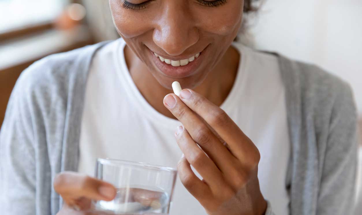 woman holding a glass of water taking a hair supplement pill