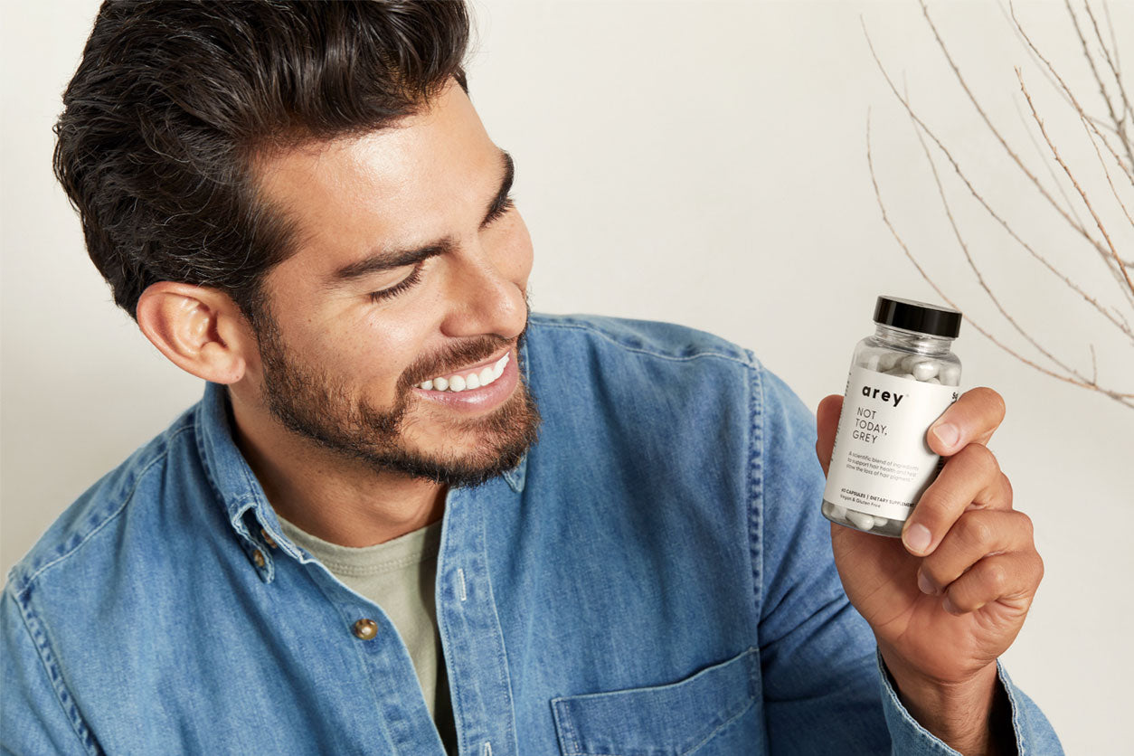 Smiling man with dark hair looks at Arey Not Today, Grey hair supplement