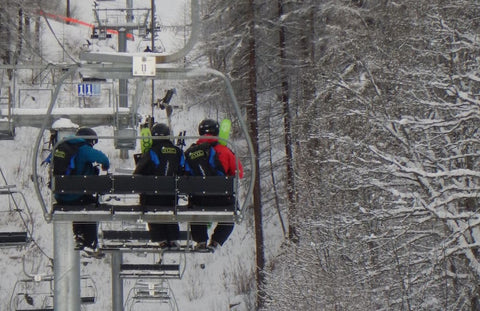 three adults on a chairlift with their Snooc sled