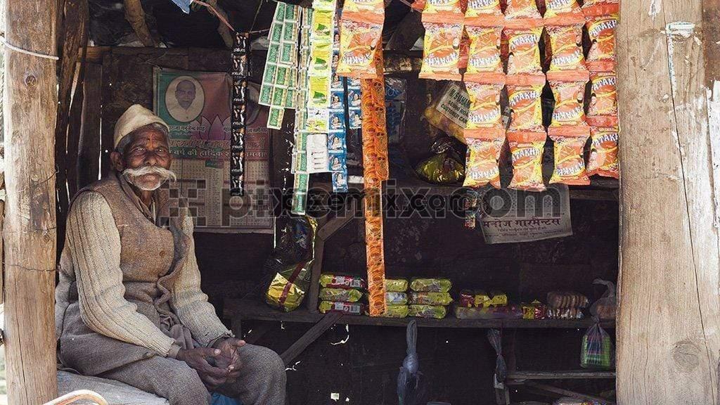 Candid portrait of an Indian shopkeeper sitting side a shop image