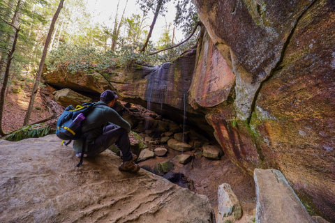 hiker sitting atop boulder overlooking whittleton arch in red river gorge kenucky