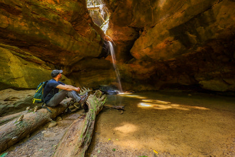 Hiker sitting beside lower falls of Conkles creek waterfall in Conkles hollow state nature preserve in Hocking county Ohio 