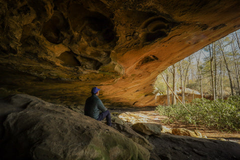 hiker sitting inside of council chamber rock shelter inside of red river gorge Kentucky 