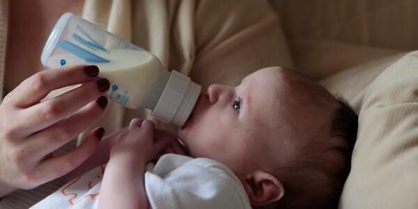 Baby being fed a half full baby formula bottle as they lay down