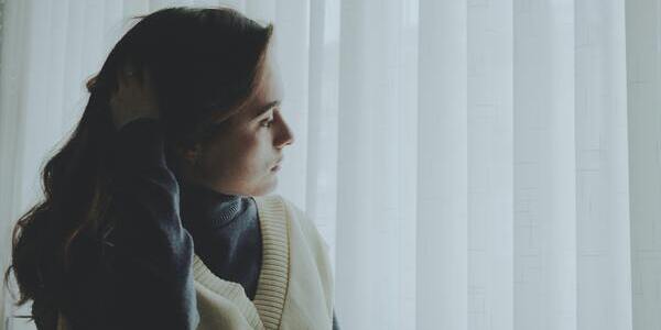 A woman conerned thinking next to a curtain scratching her head