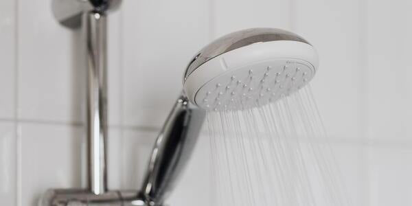 Running shower head on a white shower wall