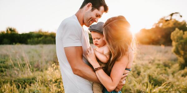 A joyful couple hugging their baby as the sunsets
