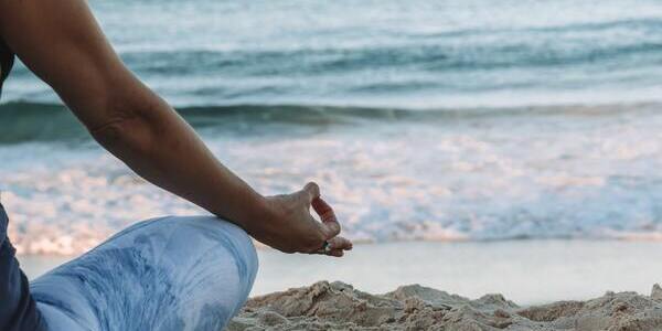 Woman sitting at the beach with her fingers in a yogic pose