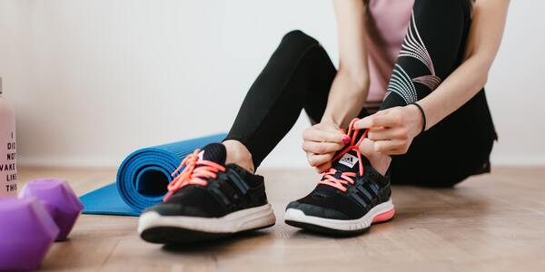 Woman tying her running shoe laces with a yoga mat and a pink weight next to her