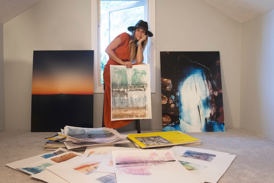 Artist Alex (Allie) Lyon standing and surrounded by her various works of art